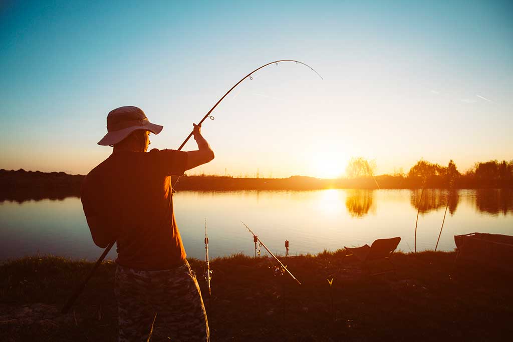 Binnengewässer Angeln Dänemark - Silhouette eines Anglers bei Sonnenuntergang, der die Ruhe und Schönheit des Angelns in einem dänischen Binnengewässer genießt.