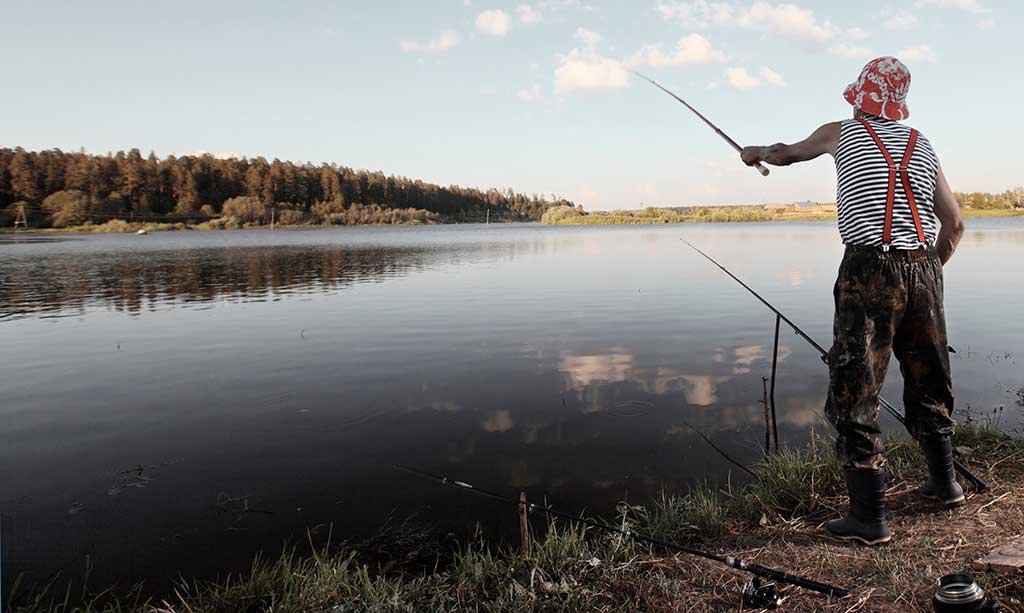 Fischreiche Jahreszeiten in Dänemark - Ein Angler in traditioneller Kleidung steht am Ufer eines ruhigen Sees und genießt die friedliche Stimmung der fischreichen Jahreszeit.