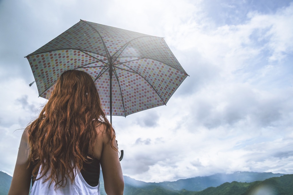 10 Tage-Wetter Dänemark – Frau mit Regenschirm blickt in die bewölkten hügelige Landschaft.