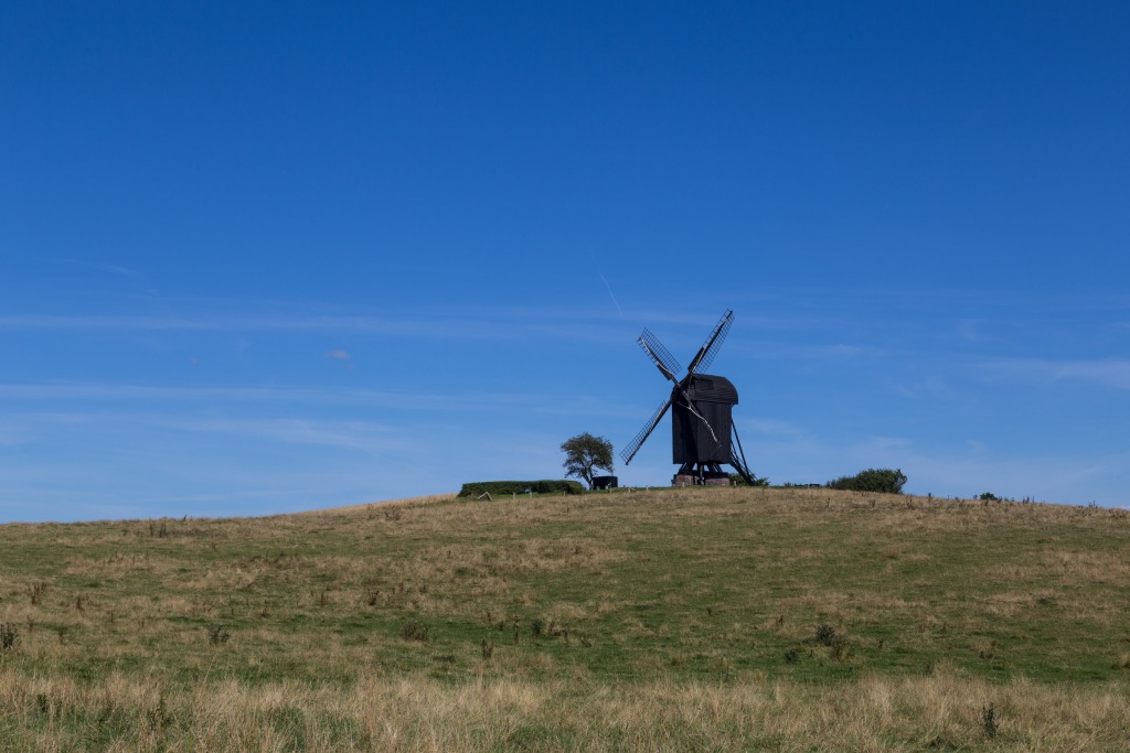 Dänemark Ferienhausanbieter - Traditionelle dänische Windmühle auf einem grünen Hügel unter einem klaren blauen Himmel, abseits der geschäftigen Städte, bietet einen friedlichen Rückzugsort.