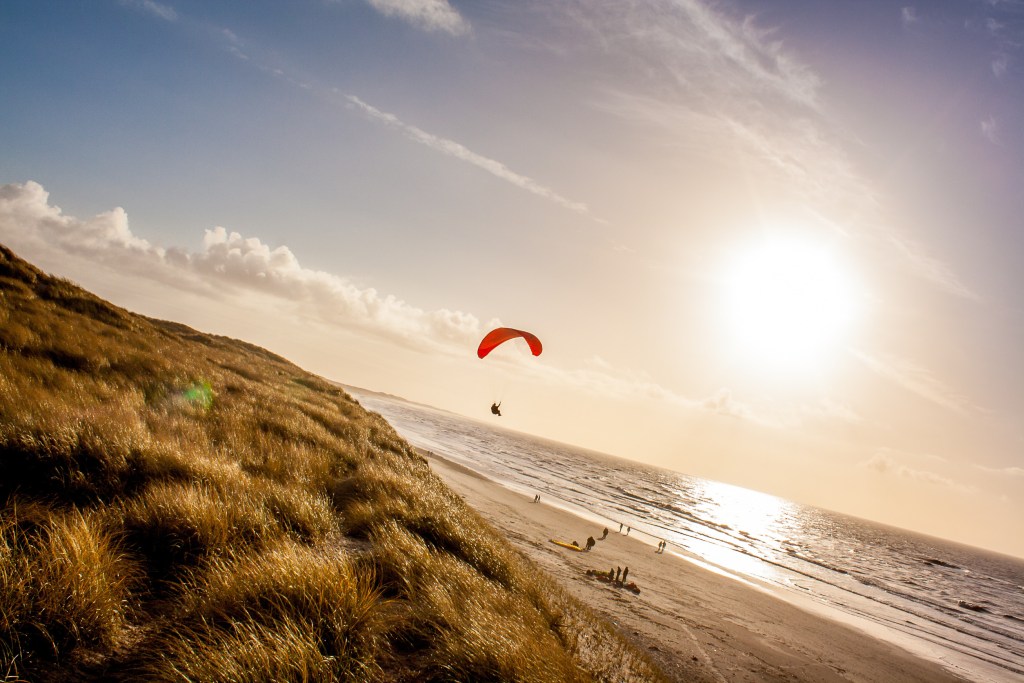 Hvide Sande Wetter - Ein Paraglider schwebt im warmen Gegenlicht der Sonne über den Dünen von Hvide Sande, ein Symbol für die dynamischen Wetterbedingungen.