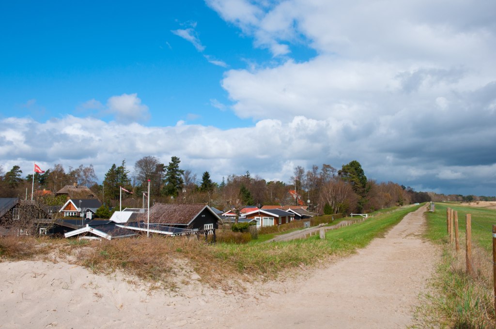 Region Marielyst - Sanfte Wellen am flachen Sandstrand mit Hintergrund der idyllischen Küstenlandschaft Marielysts.