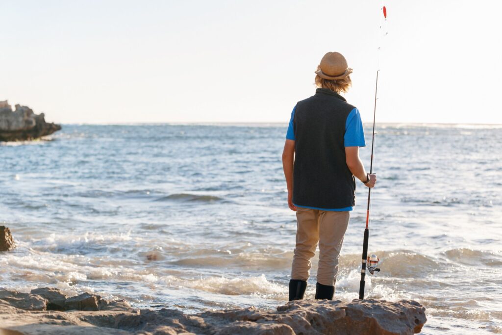 Top Angelziele in Dänemark - Ein Angler mit Strohhut steht am Meer und hält eine Angelrute, während er auf das weite Wasser blickt.