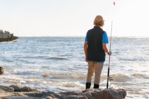 Top Angelziele in Dänemark - Ein Angler mit Strohhut steht am Meer und hält eine Angelrute, während er auf das weite Wasser blickt.