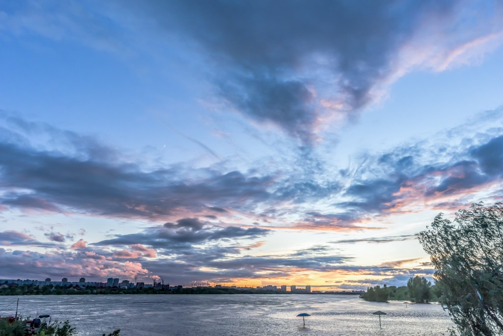 Wetter in Dänemark – Atemberaubender Sonnenuntergang mit dramatischen Wolkenformationen über dem Fluss.