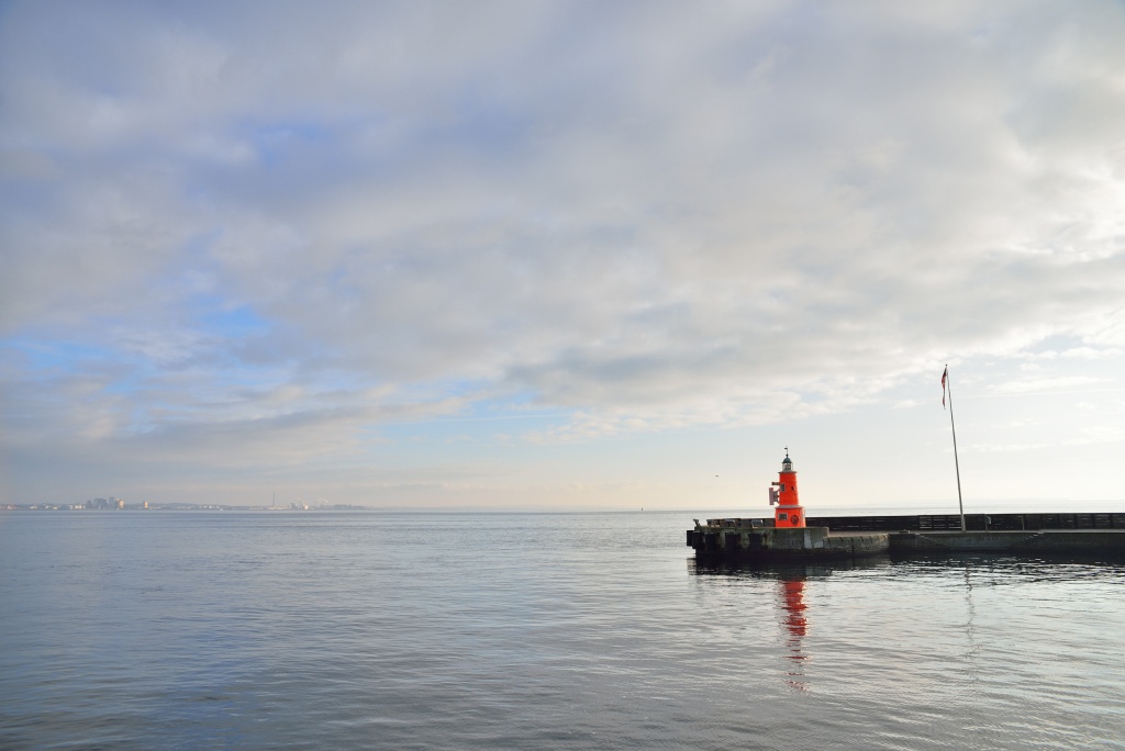 Bjerregård Wetter - Ruhige See mit einem rot-weißen Leuchtturm am Pier, unter einem weiten Himmel voller zarter Wolken.