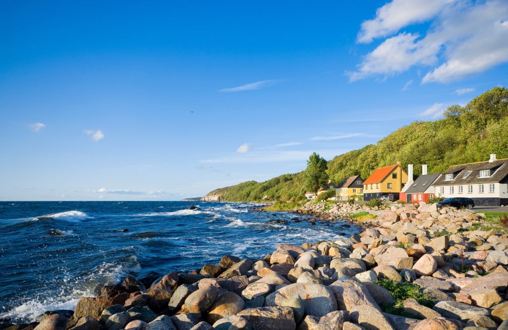 Bornholm, ein Küstendorf mit bunten Häusern entlang des steinigen Ufers unter einem klaren blauen Himmel.