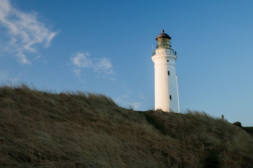Dänemark Ferienhäuser Jammerbucht - Ein majestätischer Leuchtturm, der sich über die sandigen Dünen der Jammerbucht erhebt, unter einem klaren blauen Himmel.