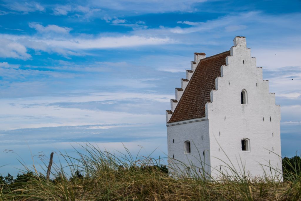 Dänemark Jammerbucht Ferienhaus - Eine malerische, weiße Kirche steht auf den Dünen der Jammerbucht, umgeben von wildem Gras und einem dramatischen Himmel.