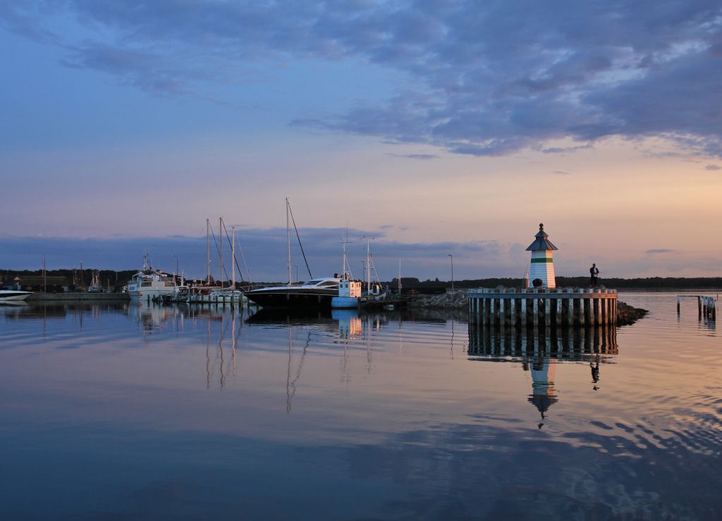 Ebeltoft Strand bei Sonnenuntergang mit ruhigem Hafen und Leuchtturm.