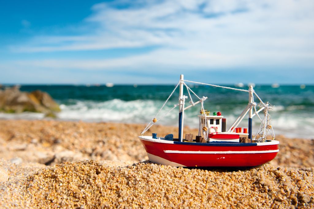 Maritimes Flair in Klegod Ferienhäuser Klegod Dänemark - Ein detailliertes Modell eines Fischerboots im Vordergrund, auf dem Kiesstrand mit dem Meer im Hintergrund, symbolisiert die maritime Kultur nahe den Ferienhäusern in Klegod, Dänemark.
