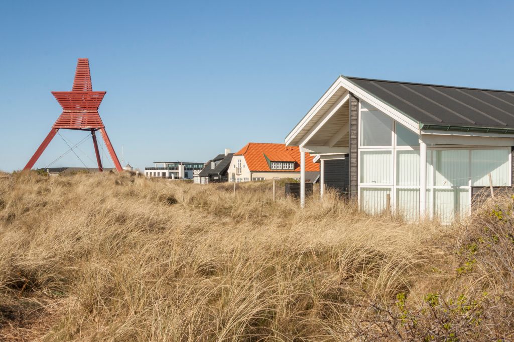 Ferienhäuser Klegod - Ein Seezeichen in Rot steht zwischen den Dünen, mit Ferienhäusern im Hintergrund unter einem klaren blauen Himmel in Klegod, Dänemark.