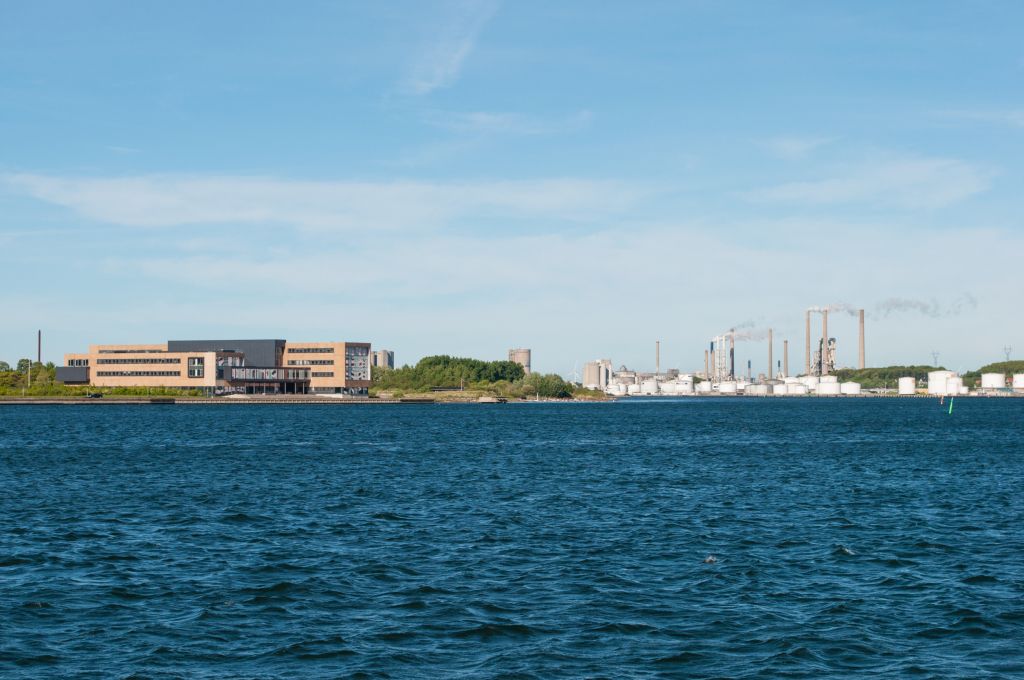 Ferienhaus Blokhus - Blick über das Wasser auf moderne Gebäude und Industrieanlagen, die eine interessante Mischung aus Arbeits- und Erholungsumgebung in Blokhus, Dänemark, darstellen.