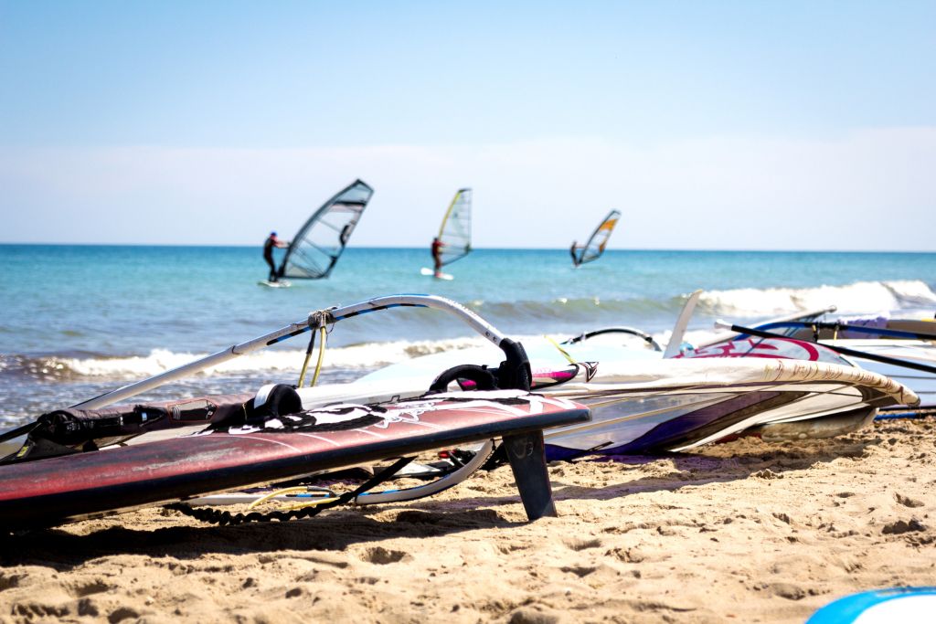 Ferienhaus Klegod Dänemark - Windsurf-Bretter liegen bereit am Strand, während im Hintergrund Surfer das Meer bei Klegod, Dänemark, genießen.