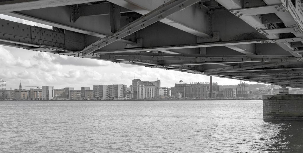 Feriepartner Blokhus - Blick auf die moderne Stadtarchitektur vom Unterbau einer Brücke über einen Fluss, in Schwarz-Weiß, was eine urbane Atmosphäre unterstreicht.
