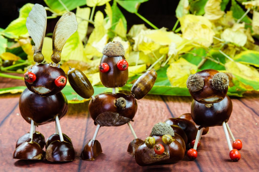 Herbstliche Bastelideen - Kreativ gestaltete Figuren aus Kastanien und herbstlichen Naturmaterialien, die Tiere darstellen, auf einem Holztisch vor einem Hintergrund aus bunten Herbstblättern.