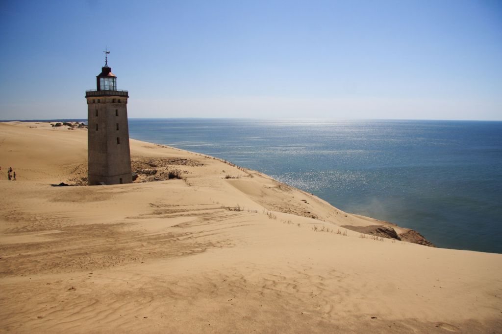 Løkken Ferienhaus – Ein einsamer Leuchtturm, der auf einer Sanddüne in Løkken thront, mit einem klaren, blauen Himmel und ruhigem Meer im Hintergrund.