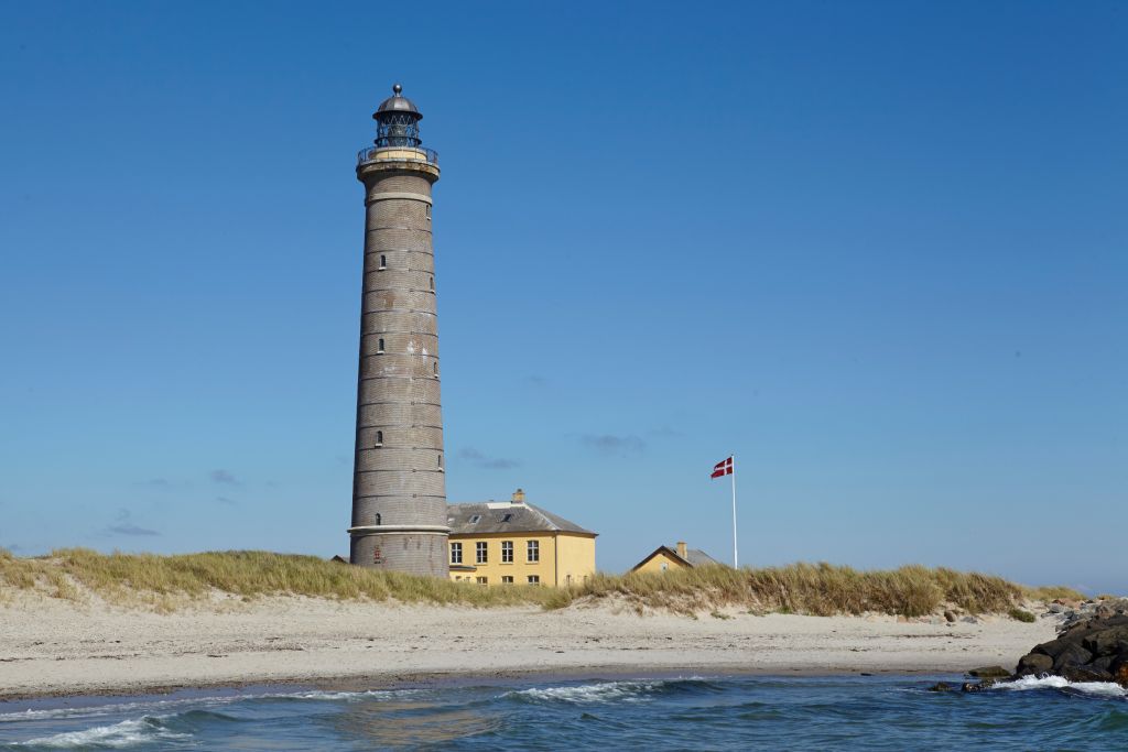 Skagen Dänemark Ferienhäuser – Der historische Leuchtturm von Skagen, umgeben von Sanddünen unter einem klaren blauen Himmel, symbolisiert die malerische Küstenlandschaft Dänemarks.