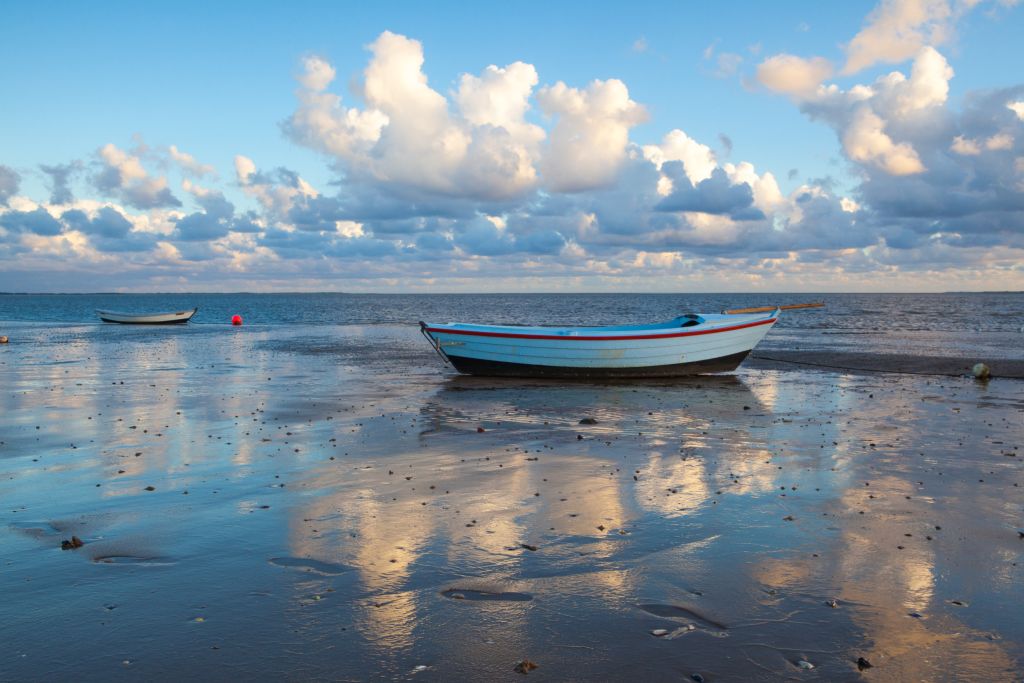 Westjütland - Zwei Boote liegen bei Ebbe auf dem nassen Sandstrand, während sich im Hintergrund der offene Himmel über dem ruhigen Meer erstreckt.